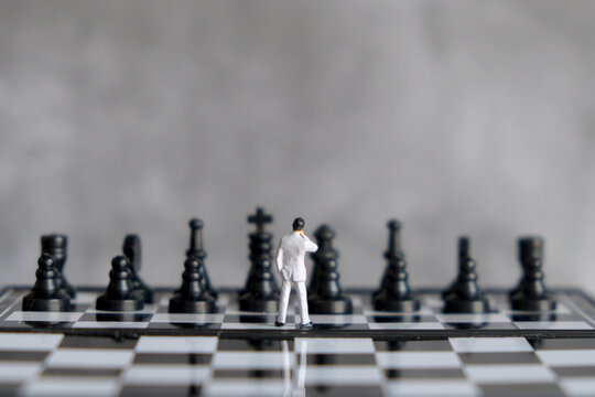 Miniature businessman standing on chessboard facing opponent pieces, business strategy, decision making, risk management, and leadership concept