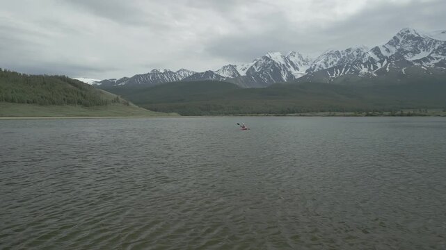Low altitude aerial shot flying forward and over a young woman paddling in a red kayak on a mountain lake, flat log profile