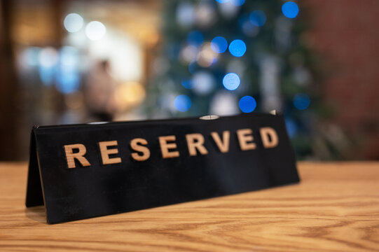 Reserved table sign on a wooden tabletop in a cozy restaurant interior with blurred Christmas tree lights in the background.