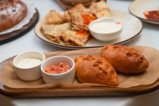 Freshly fried stuffed pies served on wooden board with sour cream and sauce, styled as traditional homemade comfort food.