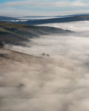View of Mam Tor rising above a thick layer of morning fog in the rolling hills of the Peak District, Hope Valley, England, United Kingdom.