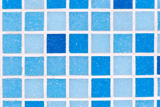 Mosaic blue tiles displaying varying shades of color and grainy texture, creating a geometric grid pattern with white grout lines, useful as a decorative surface or background