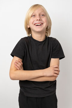 Blonde child expressing authentic happiness and childhood joy, looking upwards with a wide smile and arms crossed, standing against a clean white background
