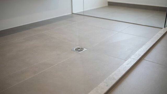 Modern gray tiled shower floor with drainage system in a minimalist bathroom design.