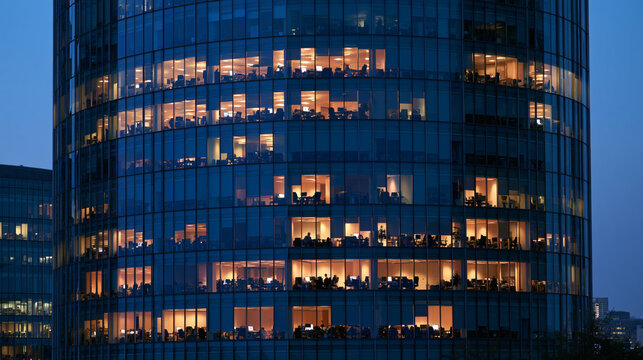 Office Building at Night: The illuminated windows of a modern office skyscraper reveal the silhouette of workers burning the midnight oil.