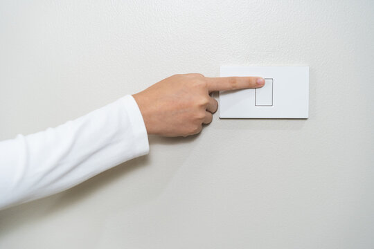 Asian young woman hand turn off on lighting switch at home room. Finger pushing light switch turn on or off white switch on wall for saving, control power electrical energy, eco environment concept.