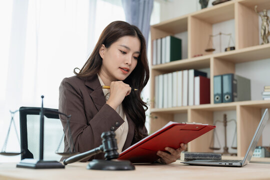 Professional female attorney sitting at desk knocking gavel while working on legal documents and laptop in office.
