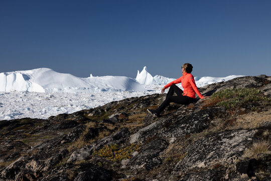 Woman in red jumper sitting in nature enjoying the views on giant icebergs in the nature in Ilulissat, Greenland