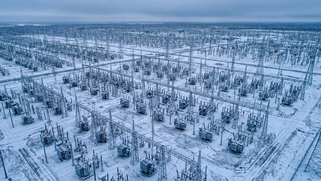 Aerial view of electrical substation and power grid in winter, high voltage transmission towers and transformers on snowy field for electricity distribution, energy supply and utility industry