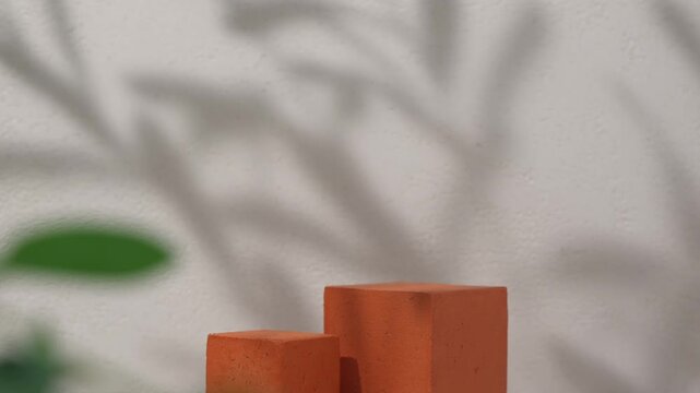 Terracotta textured cube podium placed side by side against a beige textured wall with a leaf shadow overlay, ideal for cosmetic product display and beauty advertising.