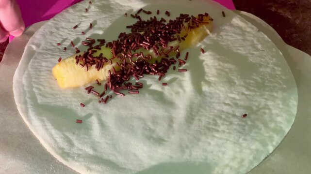 Making banana spring roll with cheese and chocolate sprinkles on spring roll wrapper