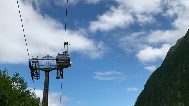 A low-angle shot of two cable cars crossing each other as they pass near a cable car pole. The sky is clear with a few white spring clouds.