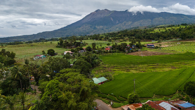 Aerial view of the majestic Mount Kanlaon volcano rising above lush green rice terraces and rural houses in Canlaon City, Negros Island Region, Philippines.