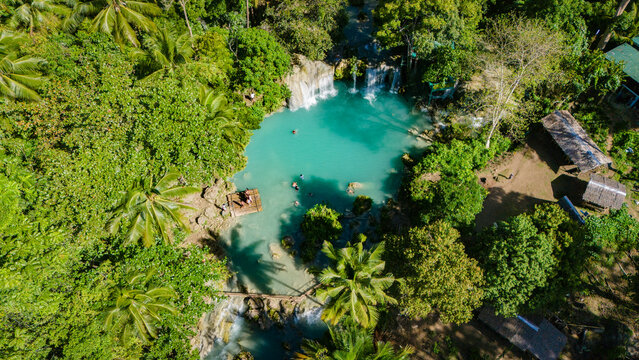 Aerial view of Cambugahay Falls with turquoise water, lush tropical forest, and people on a bamboo raft in Siquijor, Central Visayas, Philippines.