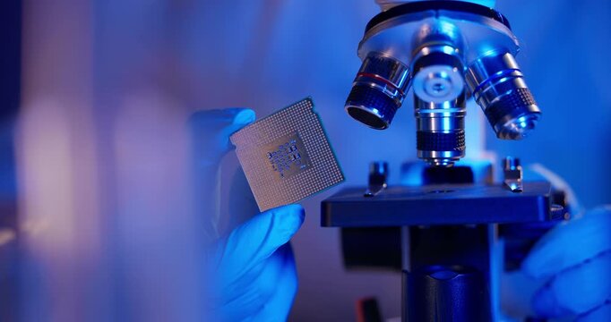 Laboratory researcher holding microchip beside microscope in lab, concept control quality on factory semiconductor.