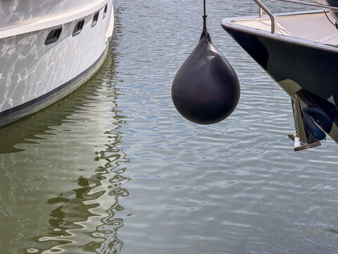 Black Spherical Boat Fender Hanging Between Two Moored Yachts in Antwerp, Belgium Marina