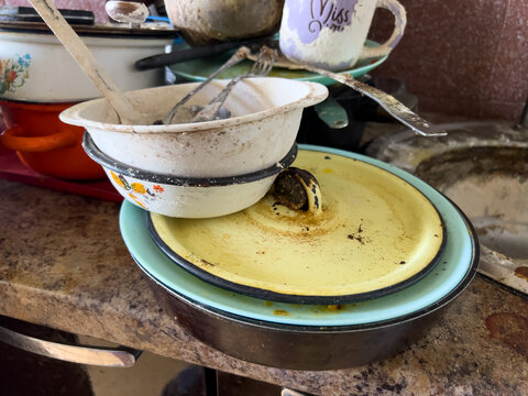 Vintage enamel cookware and kitchenware stacked on a worn countertop. The image represents abandonment, decay and forgotten everyday life