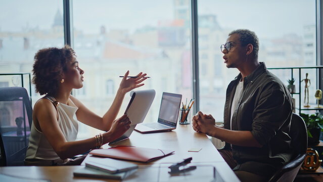 Colleagues discussing project in office meeting, woman presenting papers to man