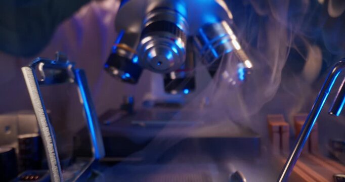Macro probe tracking shot microscope objectives descending over microchip on laboratory bench with drifting vapor and focused lighting.