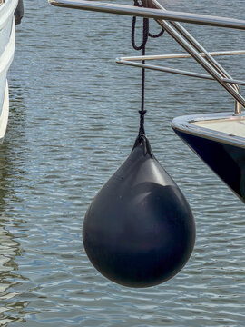 Black Teardrop Boat Fender Hanging from Yacht Railing at Marina