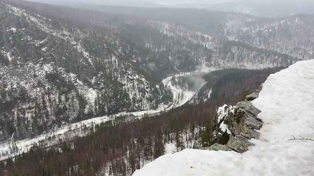 Panoramic view of frozen river, mountain ridges and train in forest.