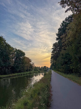 Tranquil Canal Towpath at Sunset with Tree-Lined Waterway and Dramatic Golden Sky