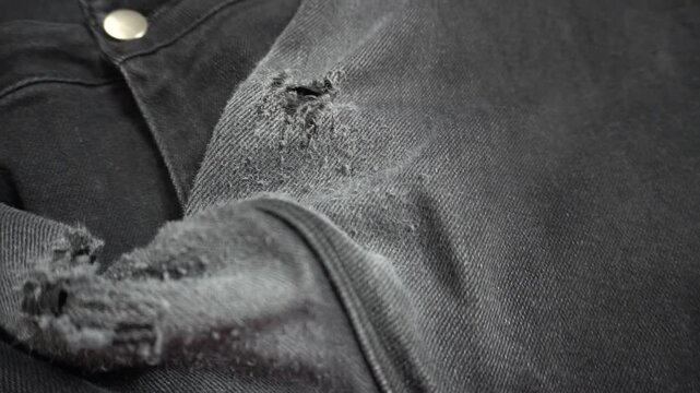 Worn gray jeans with torn holes. Ripped denim between the legs. Close-up of old, faded clothing.