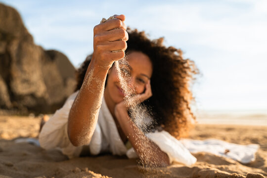 A woman playing with sand and letting it fall from her hand