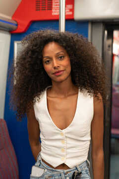 A woman with curly hair is standing inside the train in the city