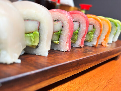 Low angle macro shot showing a line of rainbow sushi rolls topped with fresh tuna, salmon, and avocado