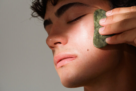 Man Using a Jade Roller on His Face in a Bright Room