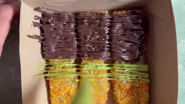 Pouring green tea matcha sauce on crispy fried banana nuggets in a paper box