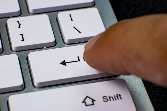 Close-up image showing a finger pressing the Enter key on a white computer keyboard. The keyboard layout includes visible keys such as Shift and bracket keys. The scene highlights interaction with com