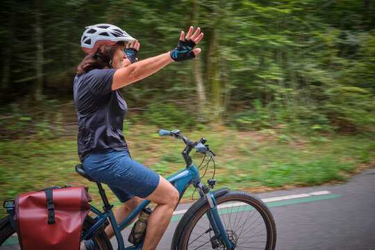 active senior woman having fun practicing handsfree cycling on a bike path through a peaceful forest, showing balance, confidence, freedom and active aging.