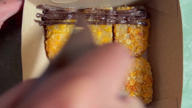Crispy fried banana nuggets drizzled with sweet chocolate sauce inside a paper box