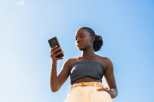Young Woman Looks at Smartphone Against Blue Sky. Copy space