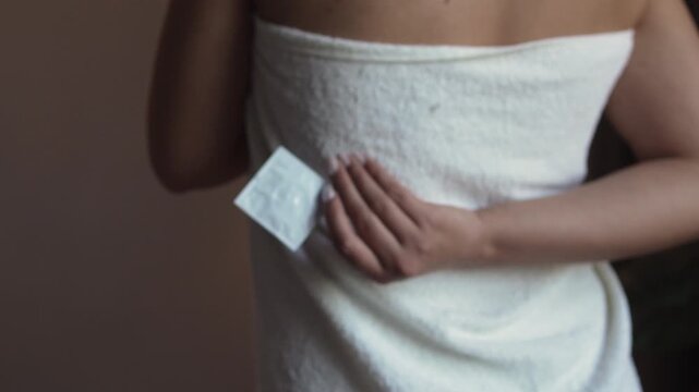 Rear view of woman wrapped in towel holds condom package in hand. contraceptive use for pregnancy prevention