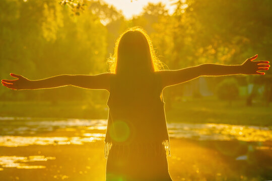 Young girl standing with open arms in warm golden sunlight, embracing the beauty of nature and symbolizing freedom, hope, happiness, inner peace and a positive new beginning. Horizontal image