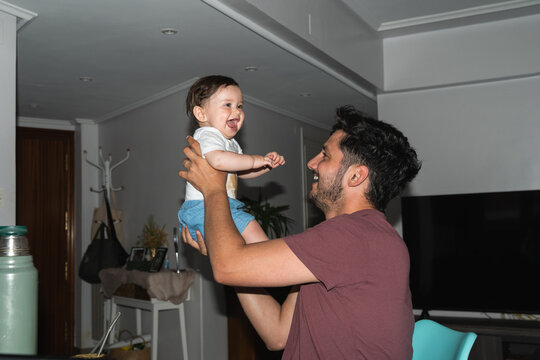 Father Lifts Child Inside Home in Joyful Moment. The child smiles