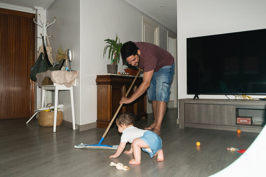 Father Cleans the Floor While Child Plays With Toys