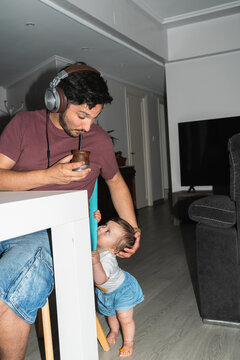 A father enjoys a drink while his baby crawls toward him at home