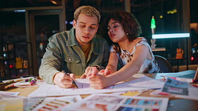 Two young designers sketching floor plan discussing project office at night