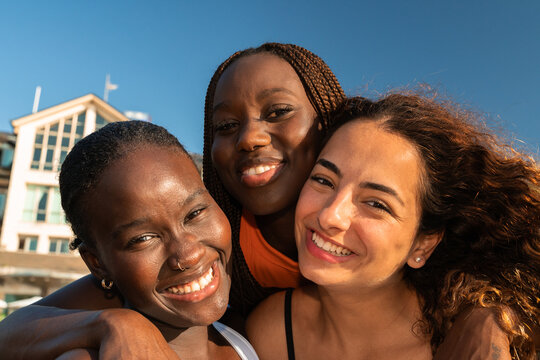 Three Women Smiling Together at the Beach During Sunny Weather