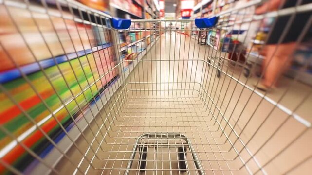 Empty metal shopping cart navigating a grocery store aisle with blurred shelves full of products, representing retail therapy, business, and the consumer journey