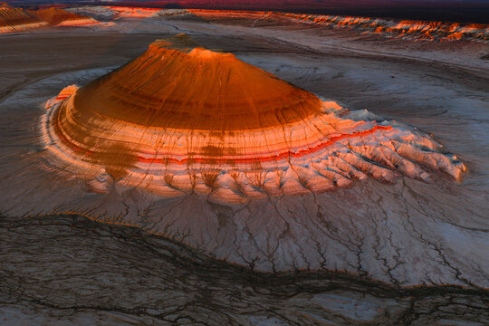 Aerial view of the colorful Gora Bokty mountain with its layered sedimentary rock formations illuminated by sunset light in the desert landscape of Karakiya District, Mangystau Region, Kazakhstan.