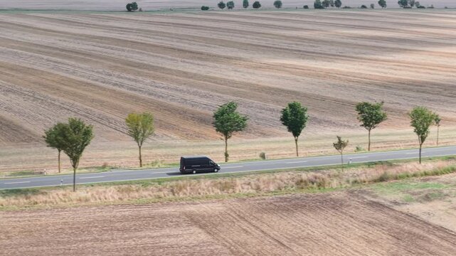 Aerial top view black modern delivery small shipment cargo courier van moving fast on motorway road city urban suburb. Business distribution and logistics express service. Mini bus driving highway day