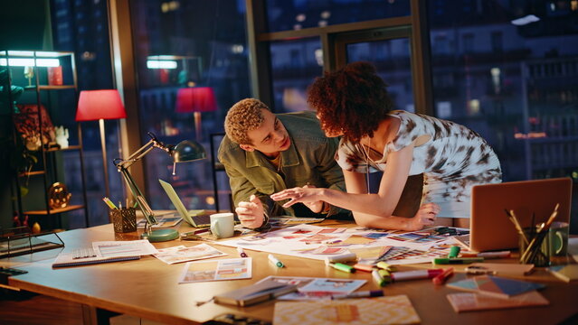 Creative couple reviewing color swatches in night studio. Designers brainstorm