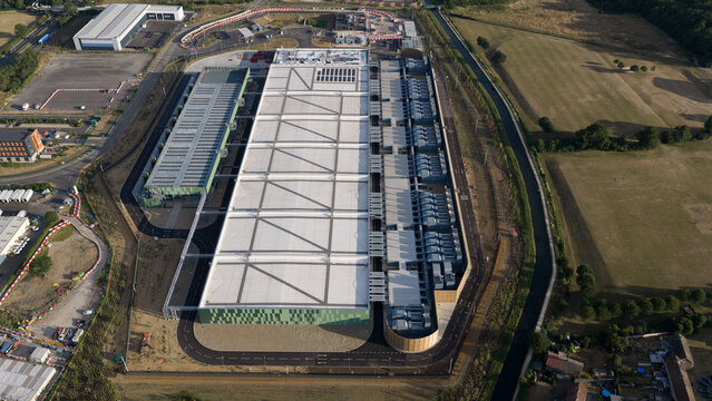 Aerial view of the Google Data Centre in Waltham Cross, featuring large industrial buildings with white roofs and access roads, surrounded by green fields in Cheshunt, England, United Kingdom.