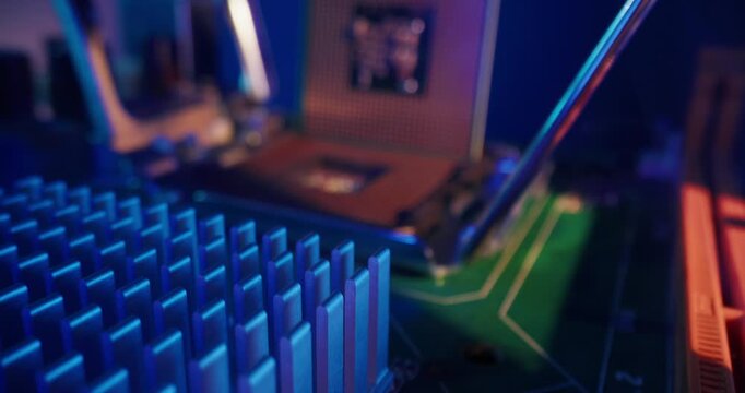 Tracking shot of cpu being inserted into motherboard socket inside desktop computer with blue purple orange studio lighting.