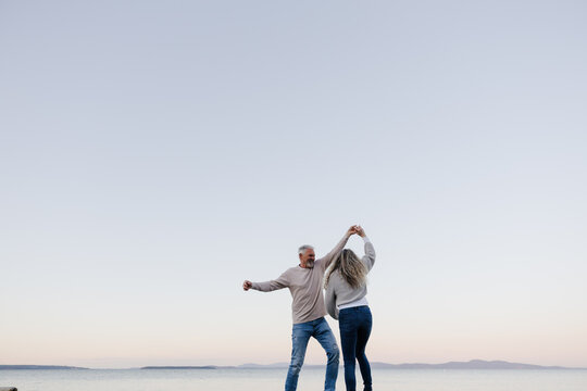 Senior couple dancing on beach at sunset in a candid joyful mome